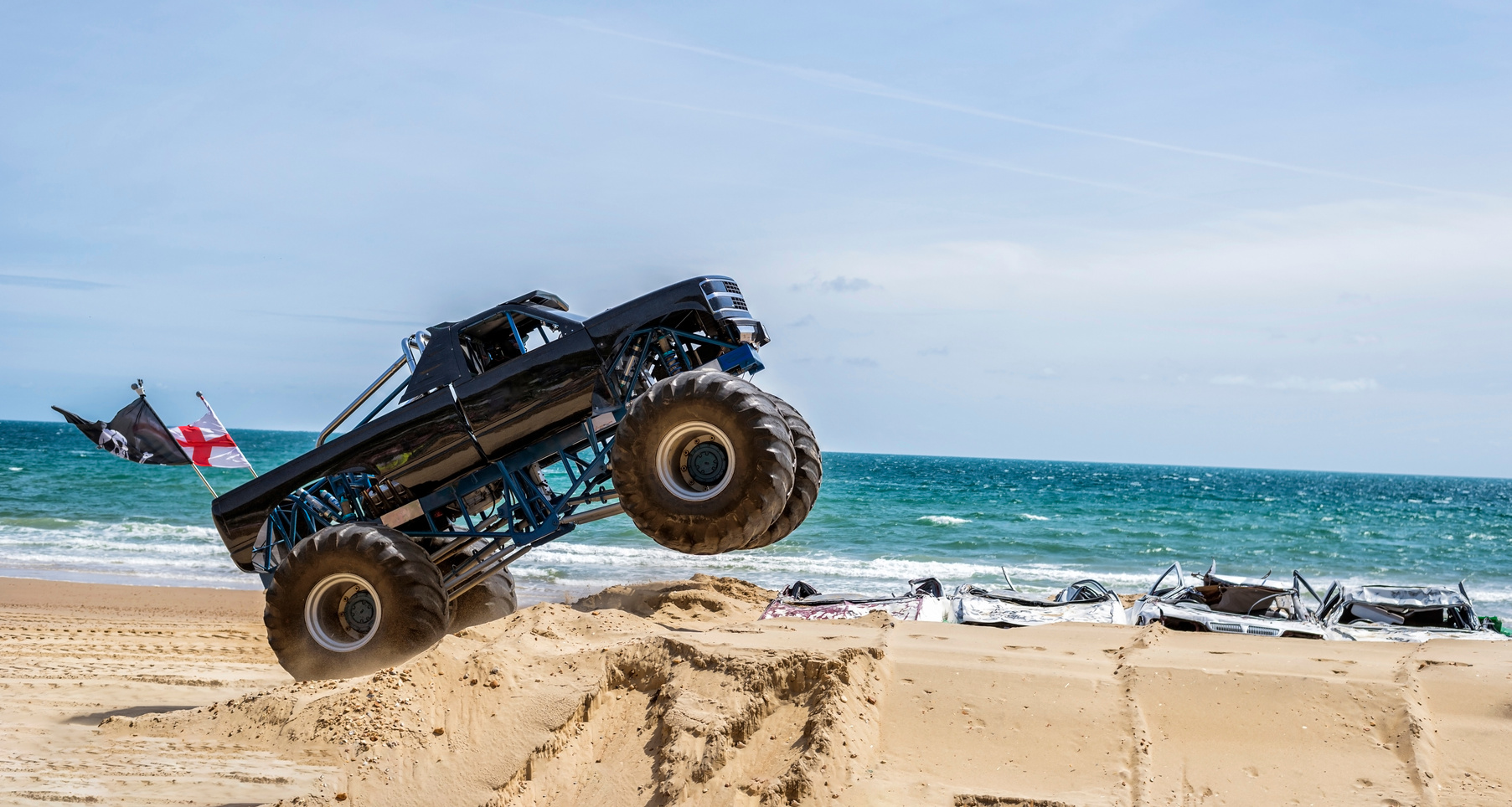 Monster truck driving over car wrecks on sandy coastal beach
